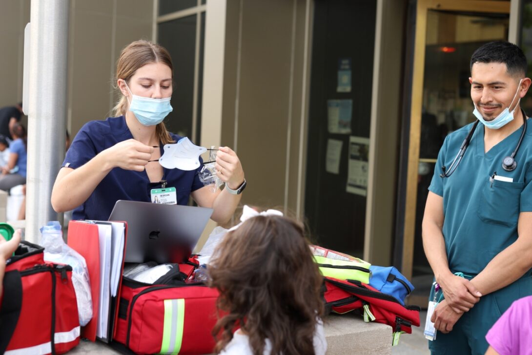 Morgan Pooler gives a mask to a child outside the District 12 police station as Dr. Alex Lucas looks on. (Photo: Jenny Fontaine/University of Illinois Chicago)