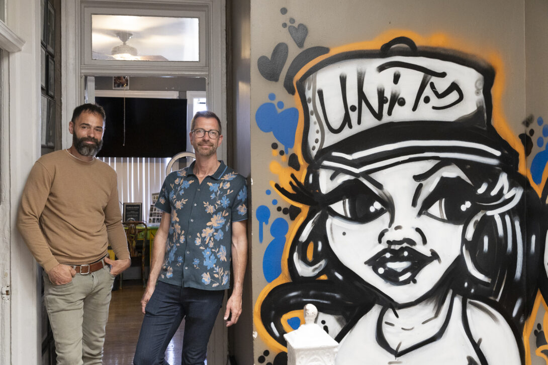 Robert Difazio and Brent Talbot standing next to a graffiti painting of a woman wearing a cap that says 