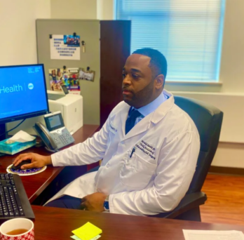 Dr. Gerald Gantt sits at his work desk in front of 3 monitors. 
